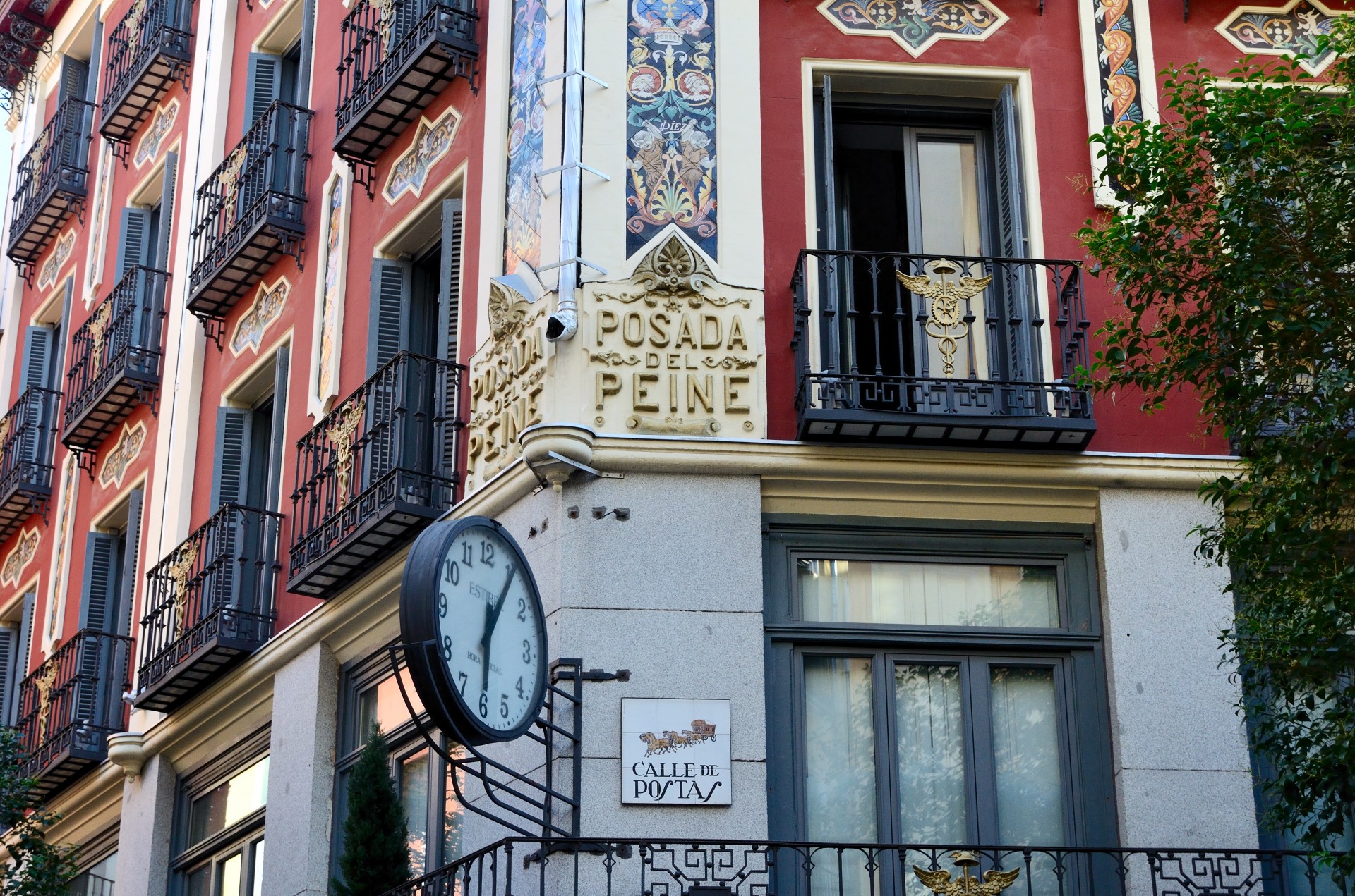 The historic Posada del Peine in Madrid, featuring a red façade, ornate tilework, wrought-iron balconies, and a distinctive street clock