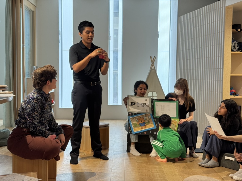 Students from May 2025 present their design work at the Neurodiversity School in Tokyo while an eager child inspects some posters.
